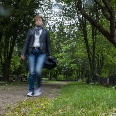 Hieman epäselvä hahmo liikkuu hautausmaan hautojen välissä kulkevaa polkua.