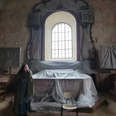 Isonkyrön kirkkoherra Satu Linko Isonkyrön vanhan kirkon alttarin luona. Alttari on peitettu liinoin, ettei se vahingoitu peruskorjauksessa. 