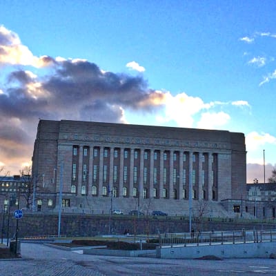 Riksdagshuset i Helsingfors fotat rakt framifrån i kvällsljus. 