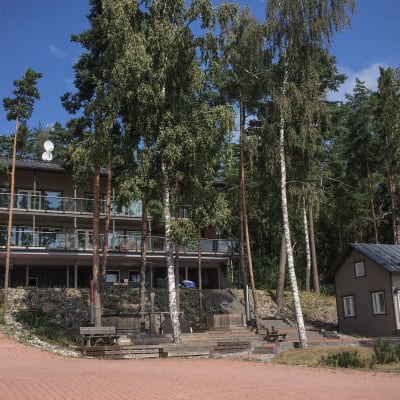 Villa Ybbersnäs, en villa i två våningar med stora fönster och balkonger med höga björkar framför. Till höger en bastu.