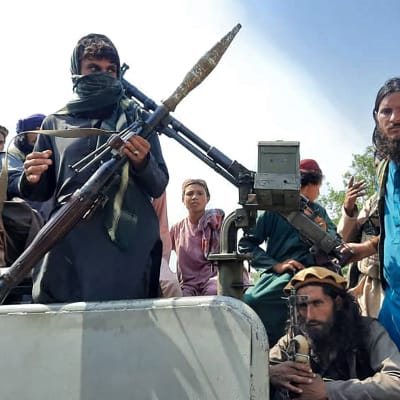 Talibaner med vapen sitter på ett fordon. 