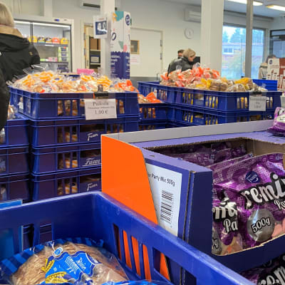 leipäkoreja joissa leipäpaketteja, karkkipusseja myyntikorissa, kaksi kassaa, ihmisiä kassoilla