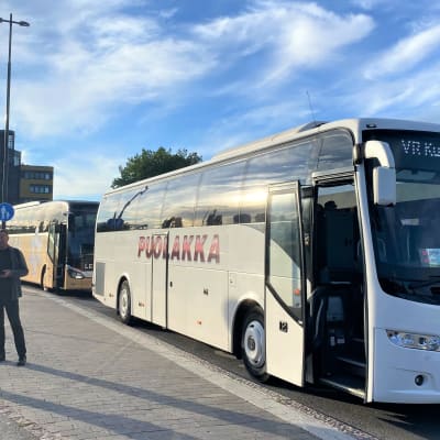 Lähikuva busseista, jotka ovat pysähtyneet Lahden matkakeskuksen laiturille. Ovet ovat auki ja matkustajia odottaa laiturilla.