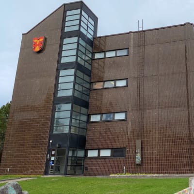 Korkea punasävyinen rakennus, edessä nurmipiha