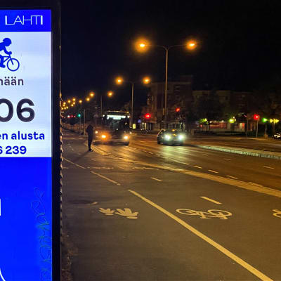 Iltakuva Lahden Uudenmaankadun pyörä- ja kävelytiestä. Kuvan etualalla on valotaulu, joka kertoo luvuin, montako pyöräilijää ja jalankulkijaa on mennyt. 