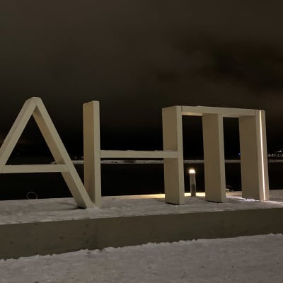 Puinen kirjainlogoteos seisoo talvisen järven rannassa. Logon teksti on Lahti. 
