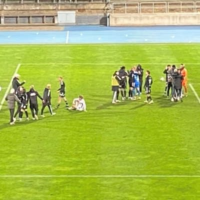 Jalkapallopelaajat halaavat toisiaan jalkapallokentällä. Osa pelaajista istuu nurmella. Lähikuva Lahden stadionin kentälle, jossa päättynyt liigakarsinta FC Lahden ja Turun Palloseuran välillä.