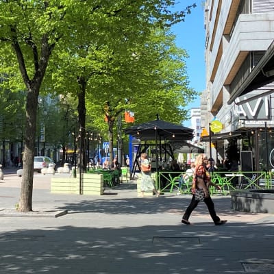 Aurinko paistaa ja ihmiset kävelevät toukokuussa Lahden keskustassa Aleksanterinkadun lähellä. Autot ajavat kadulla.