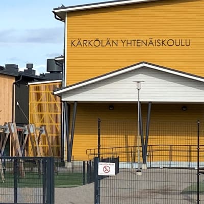 Keltainen koulurakennus, vieressä iso puinen rakennus