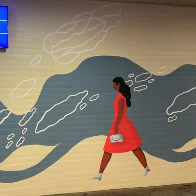 Kukkakuvio, kävelevä nainen maalattuna Lahden rautatieaseman käytävän seinään eli seinämaalaustaideteos.
