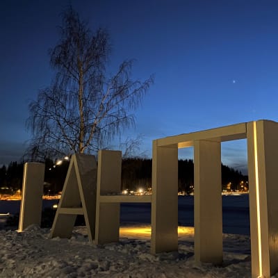 Lähikuvassa on valaistu puuteos, jossa lukee Lahti. Taustalla on jäinen Vesijärvi.