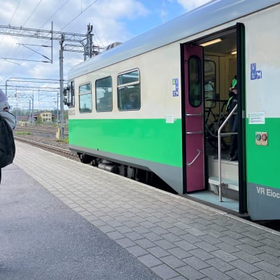 Ihminen seisoo Lahden rautatieaseman laiturilla. Vieressä on pysähtyneenä VR:n juna, jossa on ovi auki. 