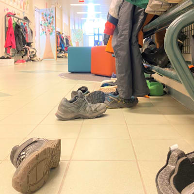 Koulun käytävä, lattialla kenkiä, naulakossa vaatteita