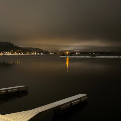 Lähikuva järvestä talvimaisemassa illalla. Järvi on Vesijärvi Lahdessa. Järven vastarannalla talojen valoja.
