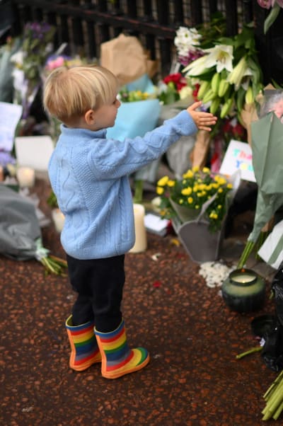 Ett barn i färgglada gummistövlar pekar mot ett blomhav utanför Buckingham Palace.