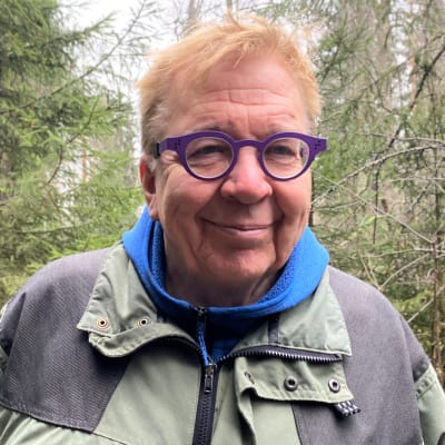 Professori Markku Ollikainen katsoo kameraan. Seisoo luontovaattet yllään keskellä metsää Lahdessa.. 