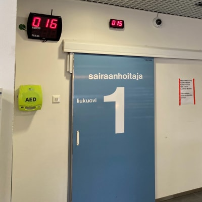 Päijät-Hämeen keskussairaalan päivystyksen vastaanoton ulko-ovia. Sairaalan käytävä ja odotusnumeroautomaatti.