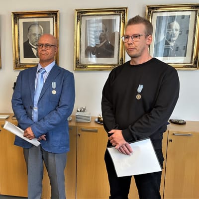 Kolme miestä seisoo aluehallintoviraston tiloissa. Seinillä tauluja Suomen entisistä presidenteistä. 
