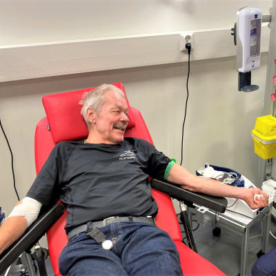 Mies luovuttaa verta Lahden veripalvelussa. Lahtelainen Pentti Attila makaa tuolissa, vieressä hoitaja valvoo luovutusta. 