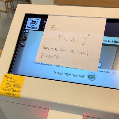 Lähikuvassa on palveluautomaatin näyttöruutu Heinolan sote-asemalla. Lappu ruudulla: Ei toimi.