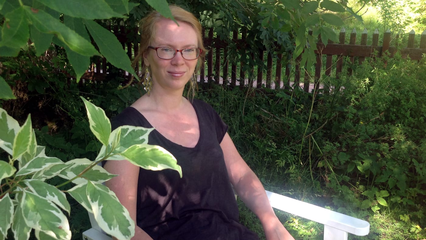 Maria Turchaninoff sits on a chair in a lush garden.