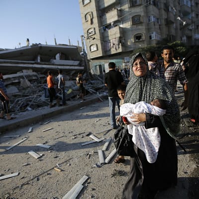 Palestinier vid ett sönderbombat hus i Gaza City den 21 juli.