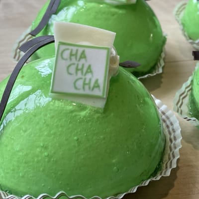 Vihreitä, puolikkaan pallon muotoisia leivoksia, joiden päällä on siivu tummaa suklaata ja valkoista suklaata, jossa lukee cha cha cha.