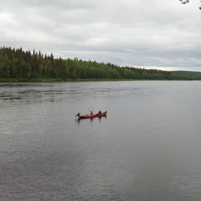 Kaksi kalastajaa joella veneessä pilvisessä säässä.