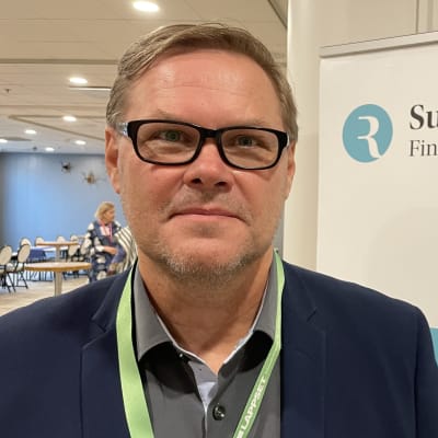 Suomen rehtorit ry:n puheenjohtaja Antti Ikonen seisoo yhdistyksen mainoksen vieressä ja katsoo kameraan.