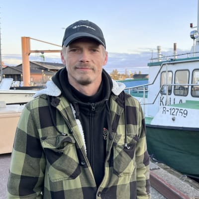 Ammattikalastaja Sami Antikainen seisoo vihreän kalastusveneensä vieressä ja katsoo kohti kameraa