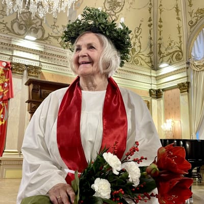 Vaasan Lucia-mummo 2022 seisoo juhlasalissa kynttiläkruunu päässään ja kukkakimppu käsissään.