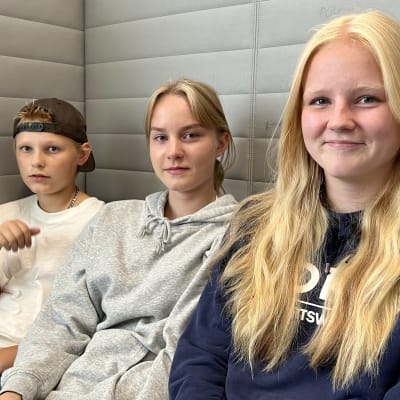 Kolme koululaista istuu sohvalla.