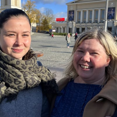 Julia Törmä ja Jaana Jämsén katsovat hymyillen kameraan. Taustalla näkyy aurinkoinen Keskustori.