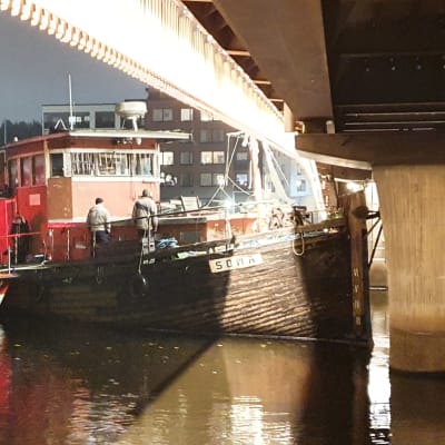 20-metrinen vene törmäsi Pielisjoella olevaan Ylisoutajan siltaan. Pelastuslaitos on irrottamassa alusta pimeänä lokakuisena iltana .