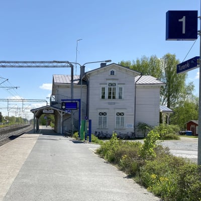 Turengin vaalea, puinen asemarakennus junaradan vieressä aurinkoisena toukokuun päivänä.