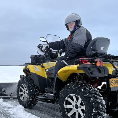 Mönkijän selässä oleva Pekka Tyllilä on kääntynyt katsomaan kohti kameraa. Taustalla näkyy jäätynyt järvi ja taivasta,