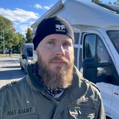 Tehyn pääluottamusmies Atte Tahvola seisoo pakettiauton edessä. Päässään musta pipo, ruskea pitkähtö parta, vihreä armeijatyylinen takki päällään. Katsoo vakavana kuvaajaa. 