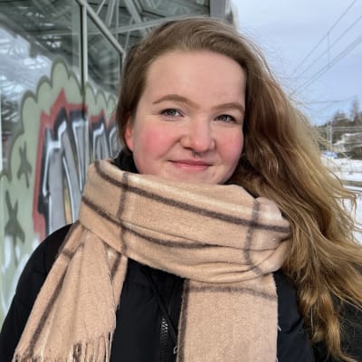 Graffiteilla maalatun seinän vierellä kameralle poseeraa Petra Varjus maaliskuisena pakkaspäivänä.