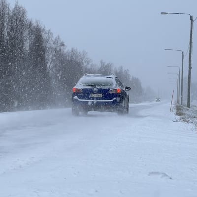 Personbil som kör på en snöig väg i snöfall. 