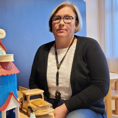  Vaasan lastensuojelun johtava sosiaalityöntekijä Tiina Böling istuu pöydän takana ja edustalla on lasten leikki-Muumitalo. 