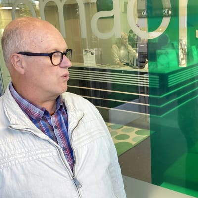 Jukka Kuivaniemi ja Anu Iso-Kokkila-Vähänen keskustelevat pankin ulkopuolella taustallaan pankin ikkunat, joista näkee pankin vastaanottotiskille.