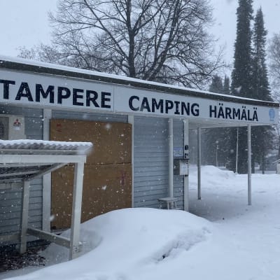 Mökin räystään alapuolella olevassa kyltissä lukee Tampere Camping Härmälä. Taustalla näkyy muita rakennuksia.