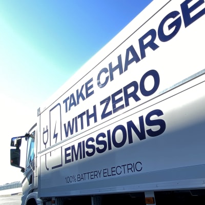 Sähkökuorma-auto kuvattuna sivusta, tavaraosan kyljessä lukee take charge with zero emissions, sininen taivas.