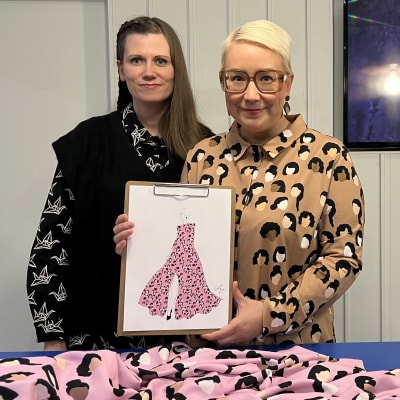 Kaksi naista esittelee Linnan juhliin suunnitellun mekon luonnosta.