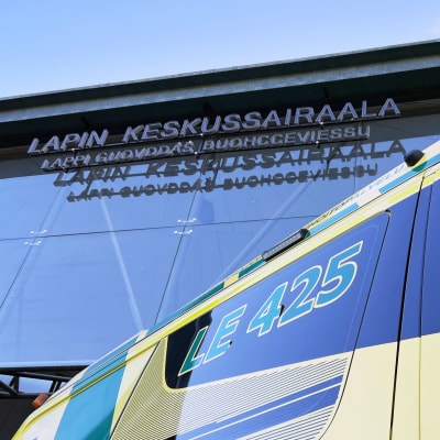 Vihreäkeltainen ambulanssin Lapin keskussairaalan edustalla. Taustalla sairaalan kyltti lasiseinällä.