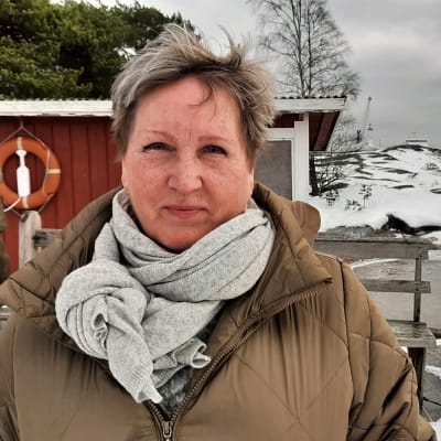 Kvinna framför röda sjöbodar vid havet.