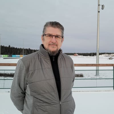 Härmän raviradan omistaja Pekka Lillbacka seisoo lumisen raviradan edessä, taustalla muun muassa ajanottorakennus.