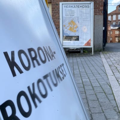 Koronarokotuskyltti tiilisen tehdaskompleksin edessä.