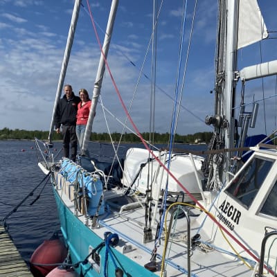 Kuvassa on purjevene kiinnitettynä laituriin, Kannella seisoo toisistaan kiinni pitäen Malin ja Janne Backlund.