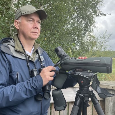 En man med keps står i ett fågeltorn med en tubkikare